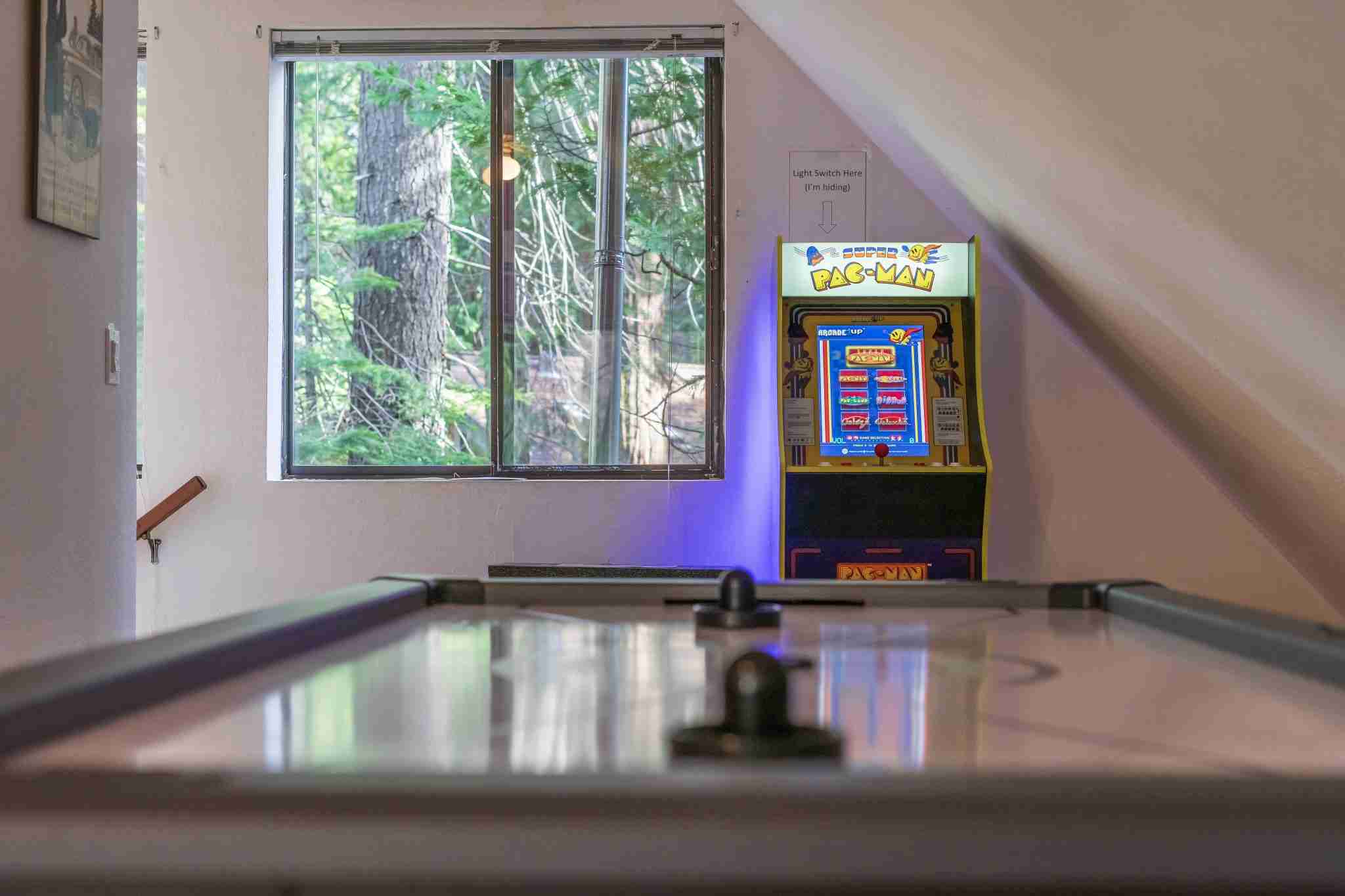 Vintage "Super Pac-Man" arcade and air hockey table near window with tree view.