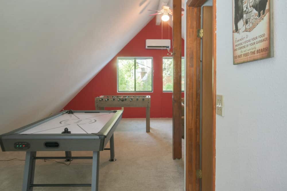 Dorrington Vacation Rental Cabins - A well-lit attic room with a slanted ceiling featuring an air hockey table, a ceiling fan, a window with a view of greenery, and decorative elements on the walls.