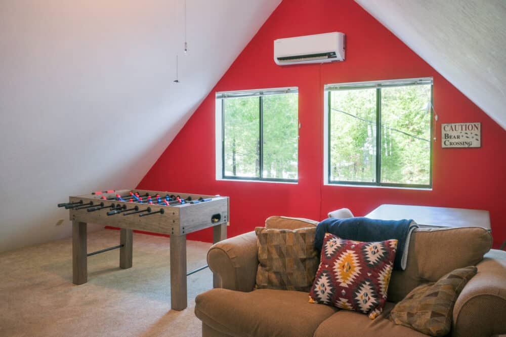 Dorrington Vacation Rental Cabins - An attic recreation room with a red wall, featuring a foosball table, a tan couch with colorful pillows, and a "caution: bear crossing" sign. frequently asked questions FAQ