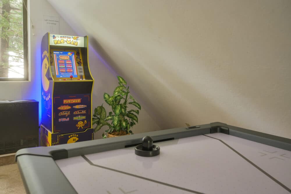 Dorrington Vacation Rental Cabins - A home recreational area featuring an air hockey table in the foreground and a classic pac-man arcade machine beside a potted plant in a well-lit room.