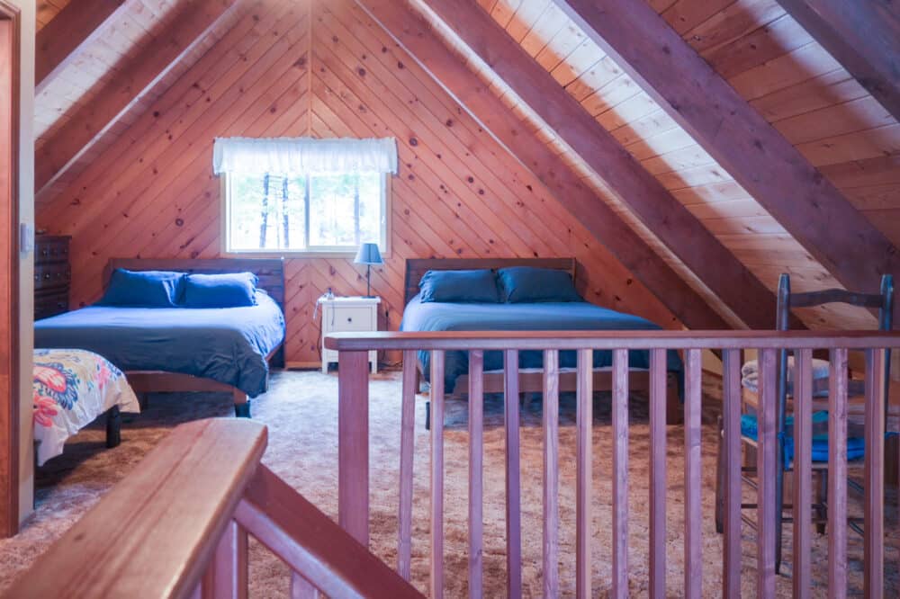 Dorrington Vacation Rental Cabins - Cozy attic bedroom with two beds and wooden interior.