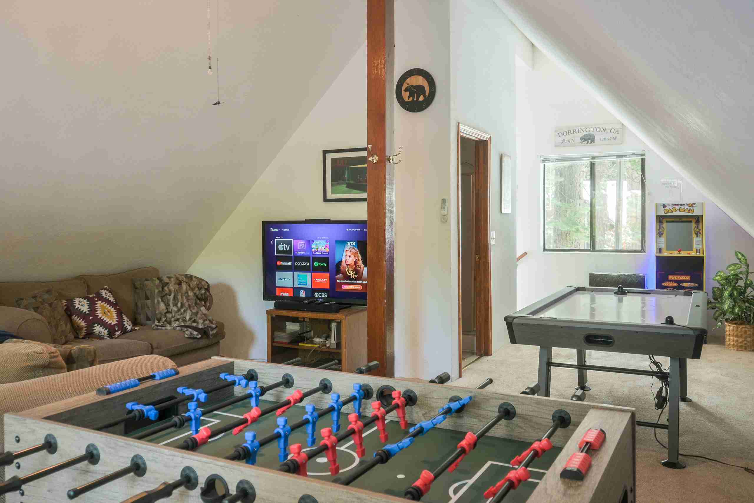 Recreational room with foosball, air hockey, arcade machine, TV, couch, window, and plant.