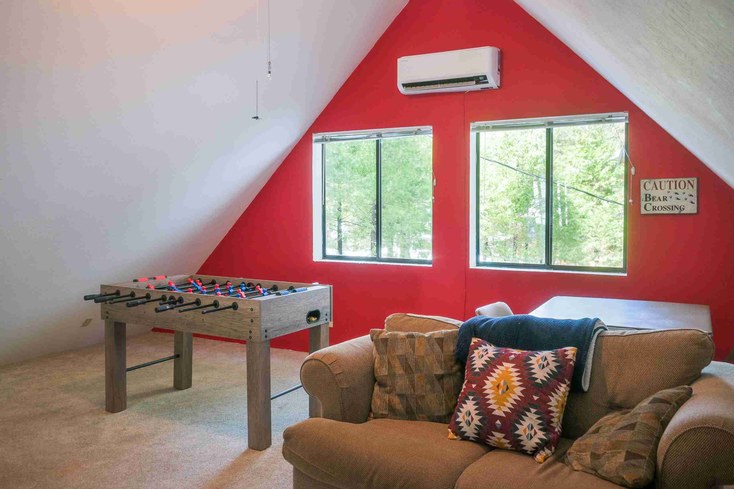 Attic room with red wall, two windows, foosball table, sofa, air conditioner, and bear sign.