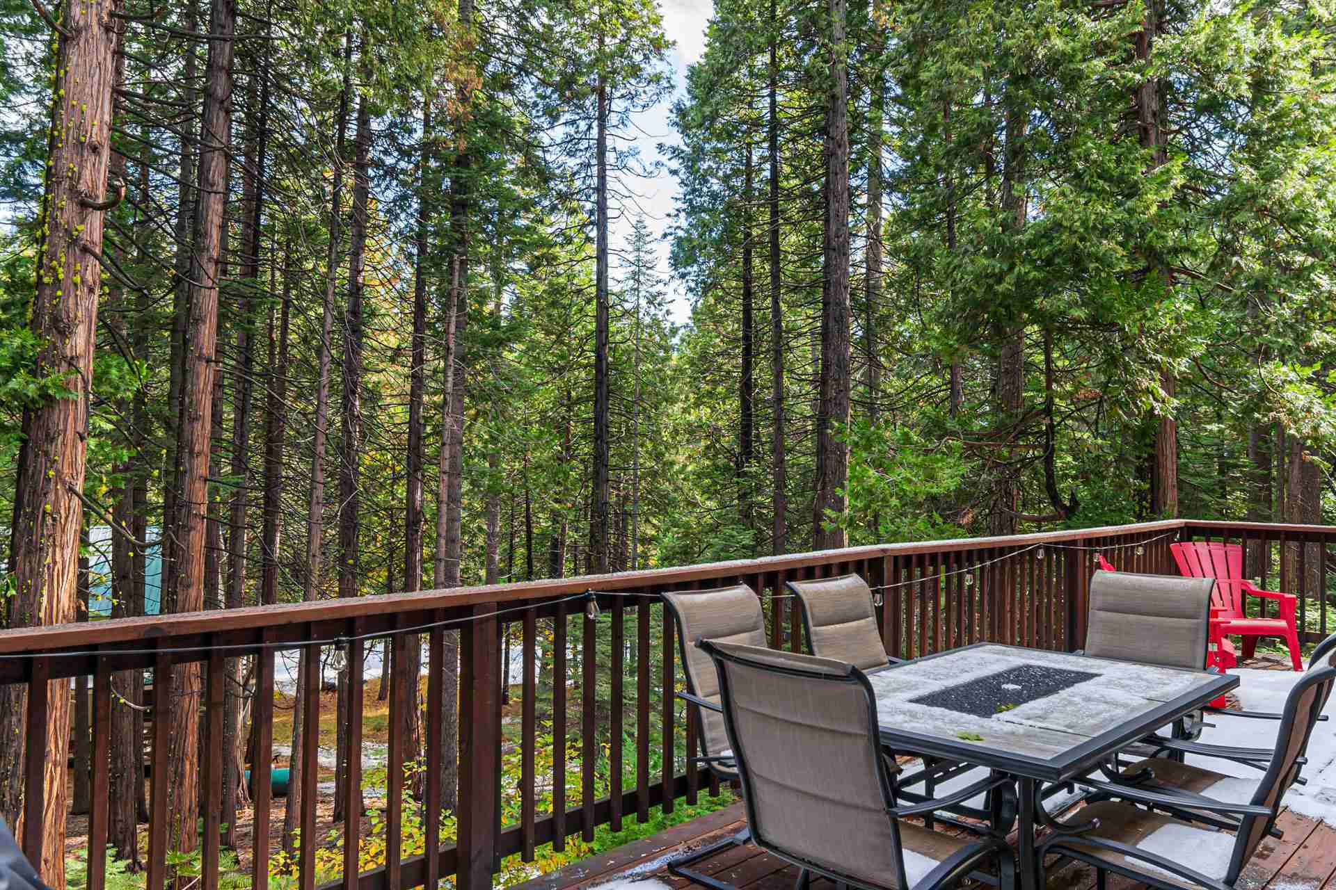 Wooden deck with outdoor dining set in a forest, featuring a red chair by the railing.