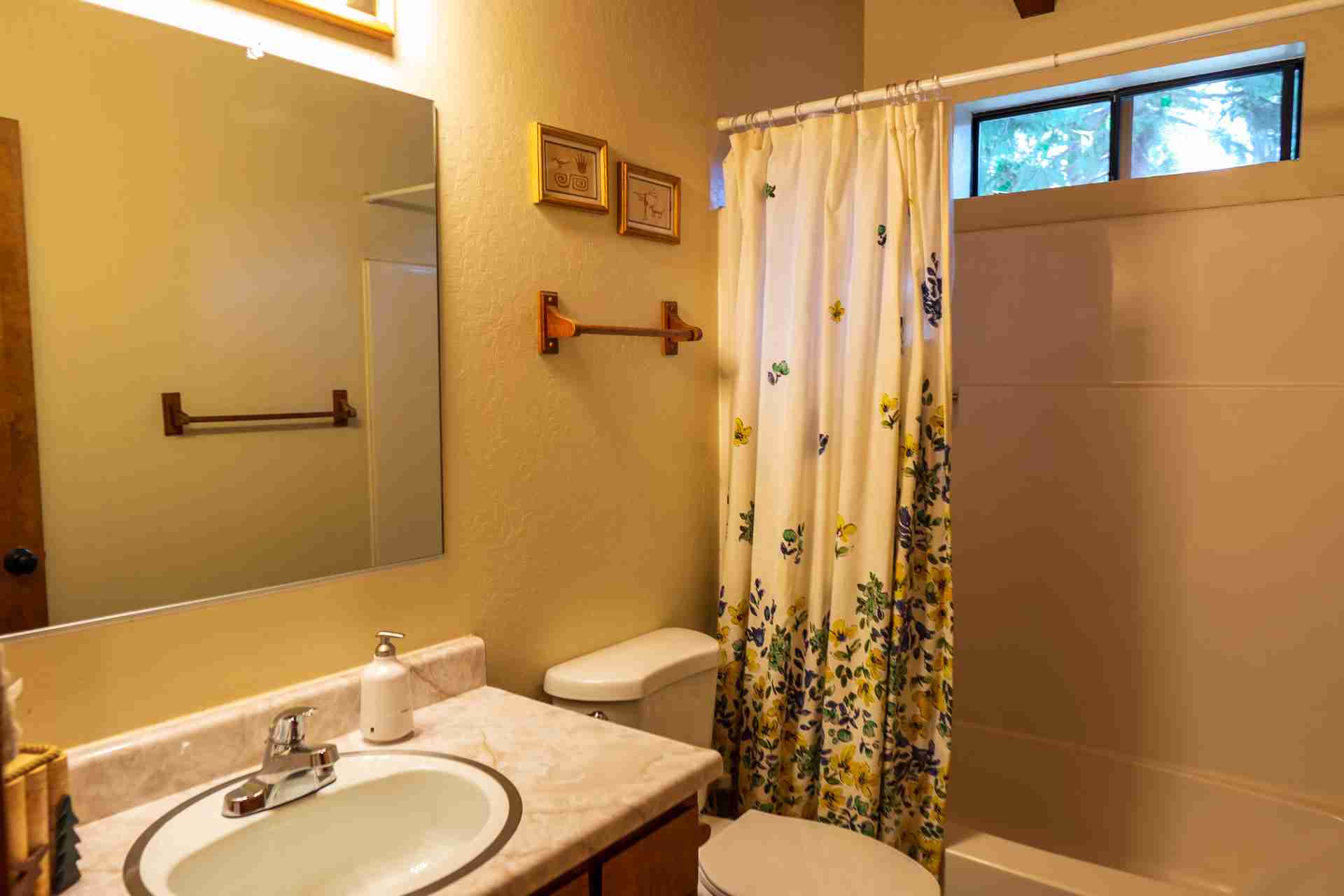 Small bathroom with sink, marble countertop, mirror, toilet, shower curtain, towel rack, window.