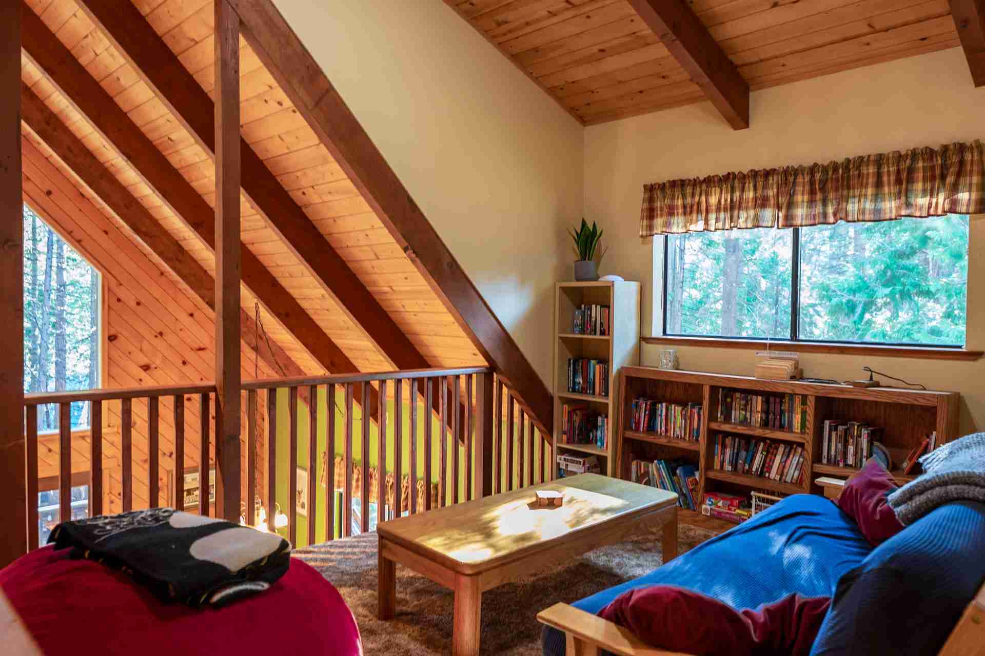 Cozy loft with beams, sloped ceiling, colorful sofa, coffee table, bookshelves, window, curtain.