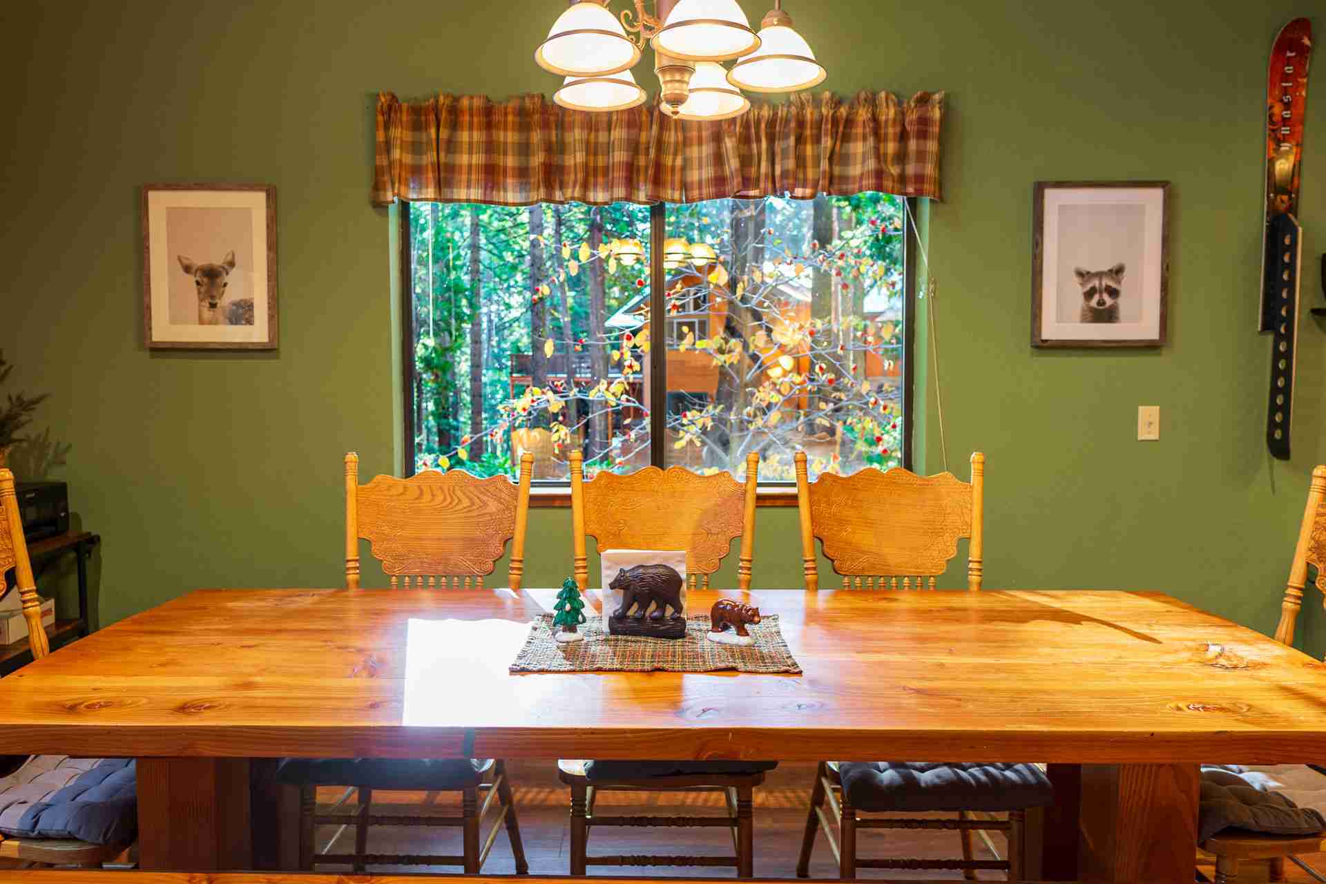 Dining room with wooden table, bear figurines, plaid curtains, and green walls with animal art.