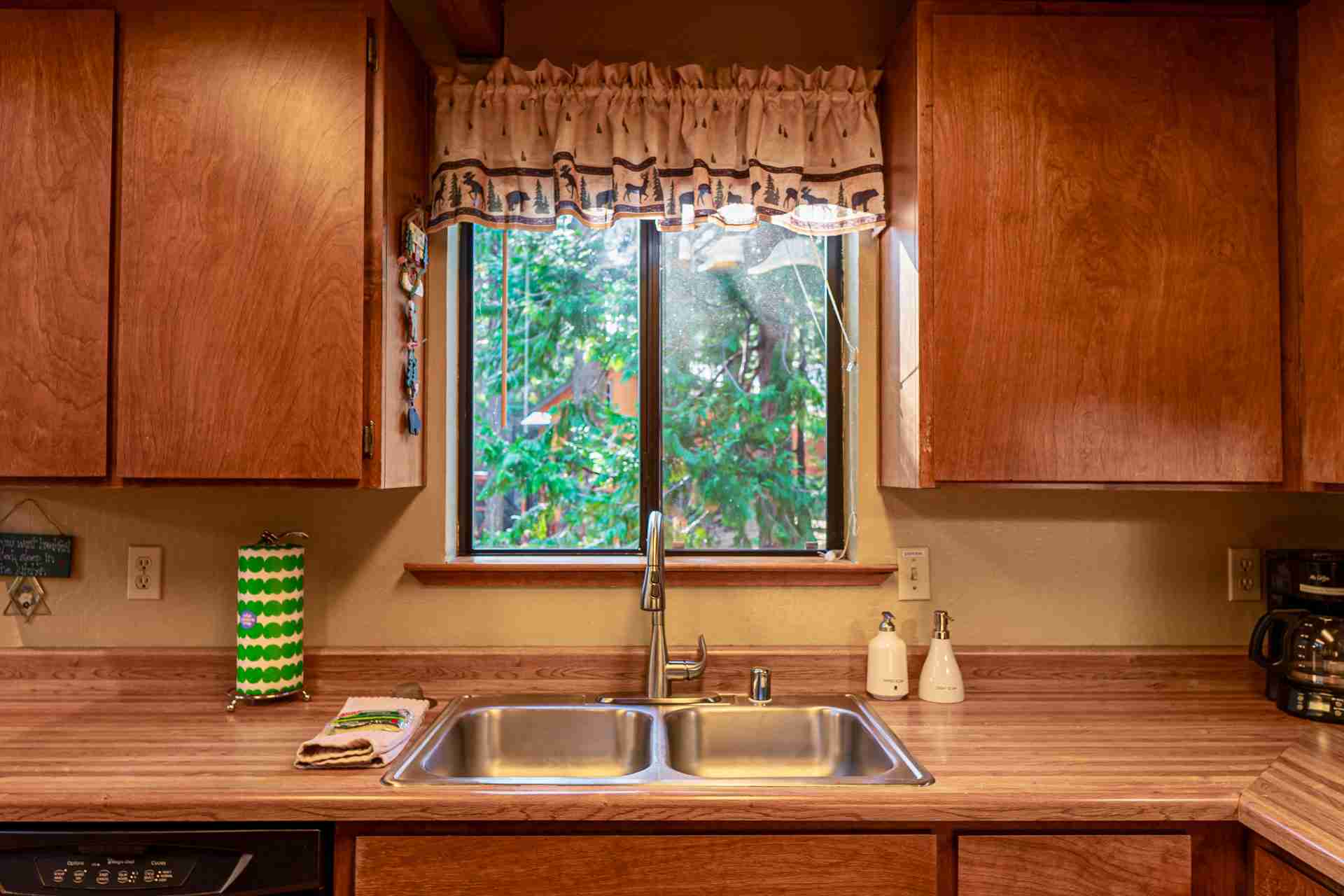 Kitchen with a double sink, nature valance, wooden cabinets, and a view of greenery.