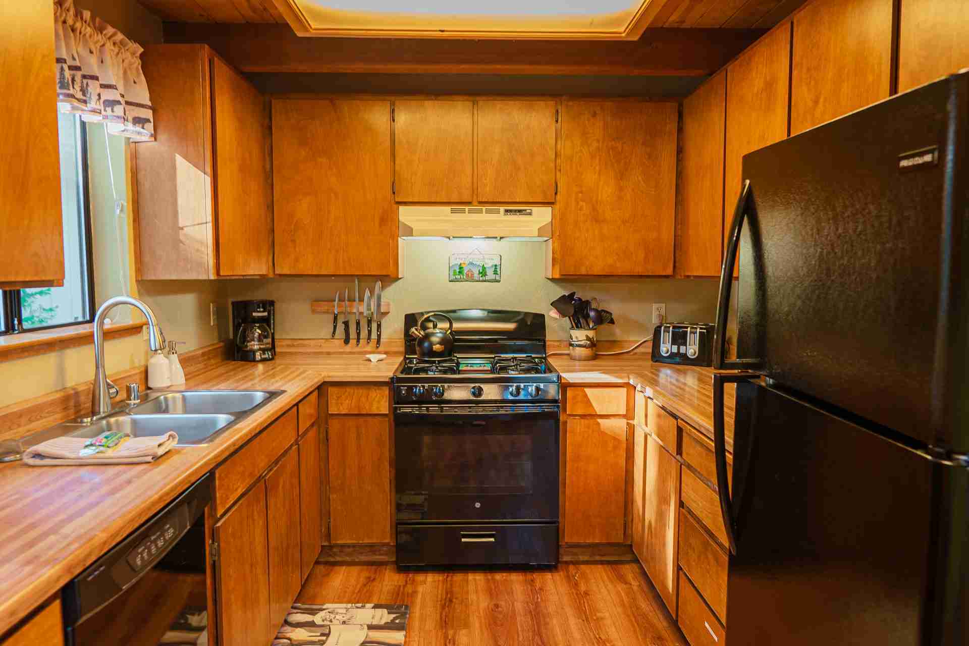 Kitchen with wooden cabinets, black appliances, utensils, and wooden flooring.