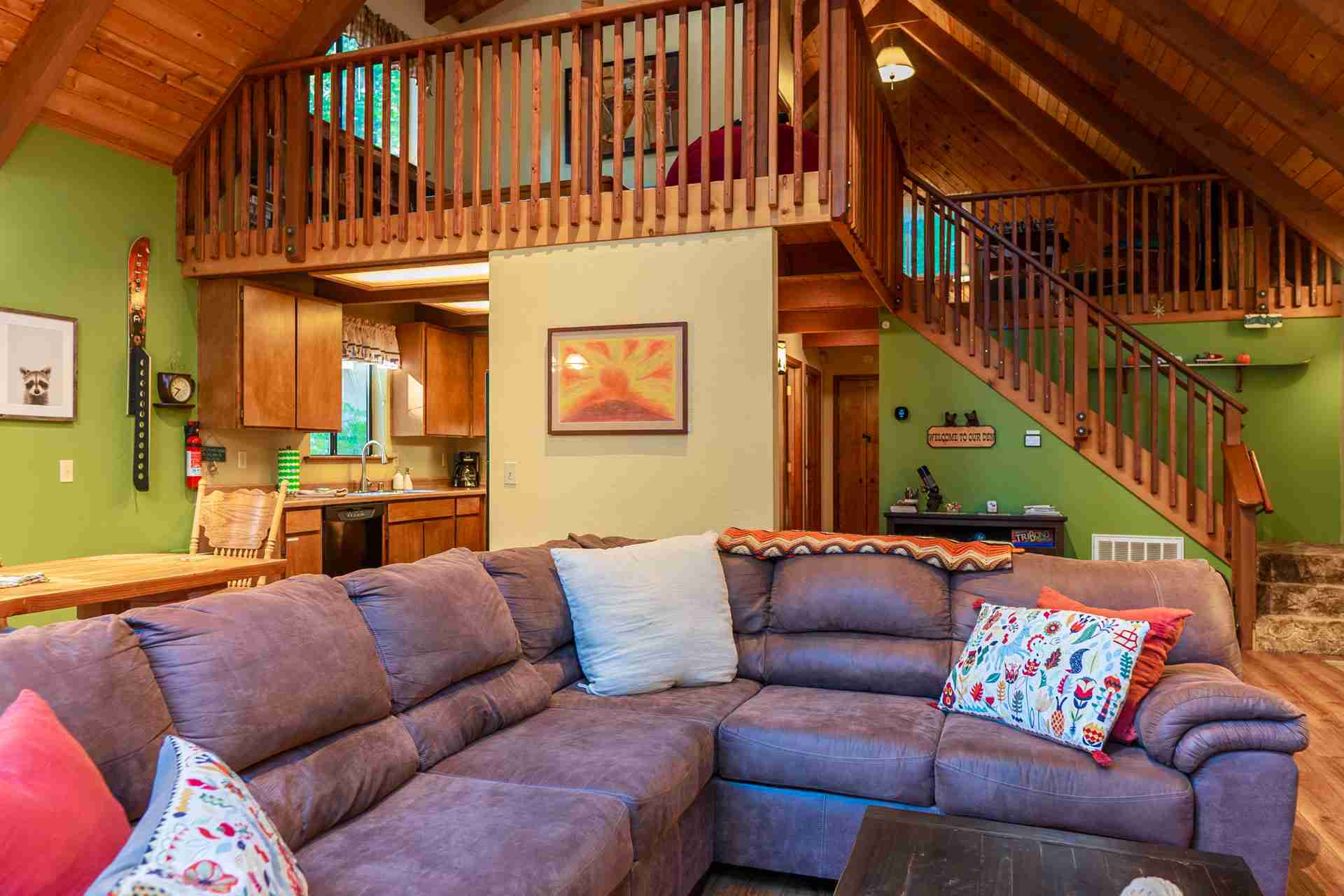 Cozy living space with a sectional sofa, rustic kitchen, and stairway to a loft.