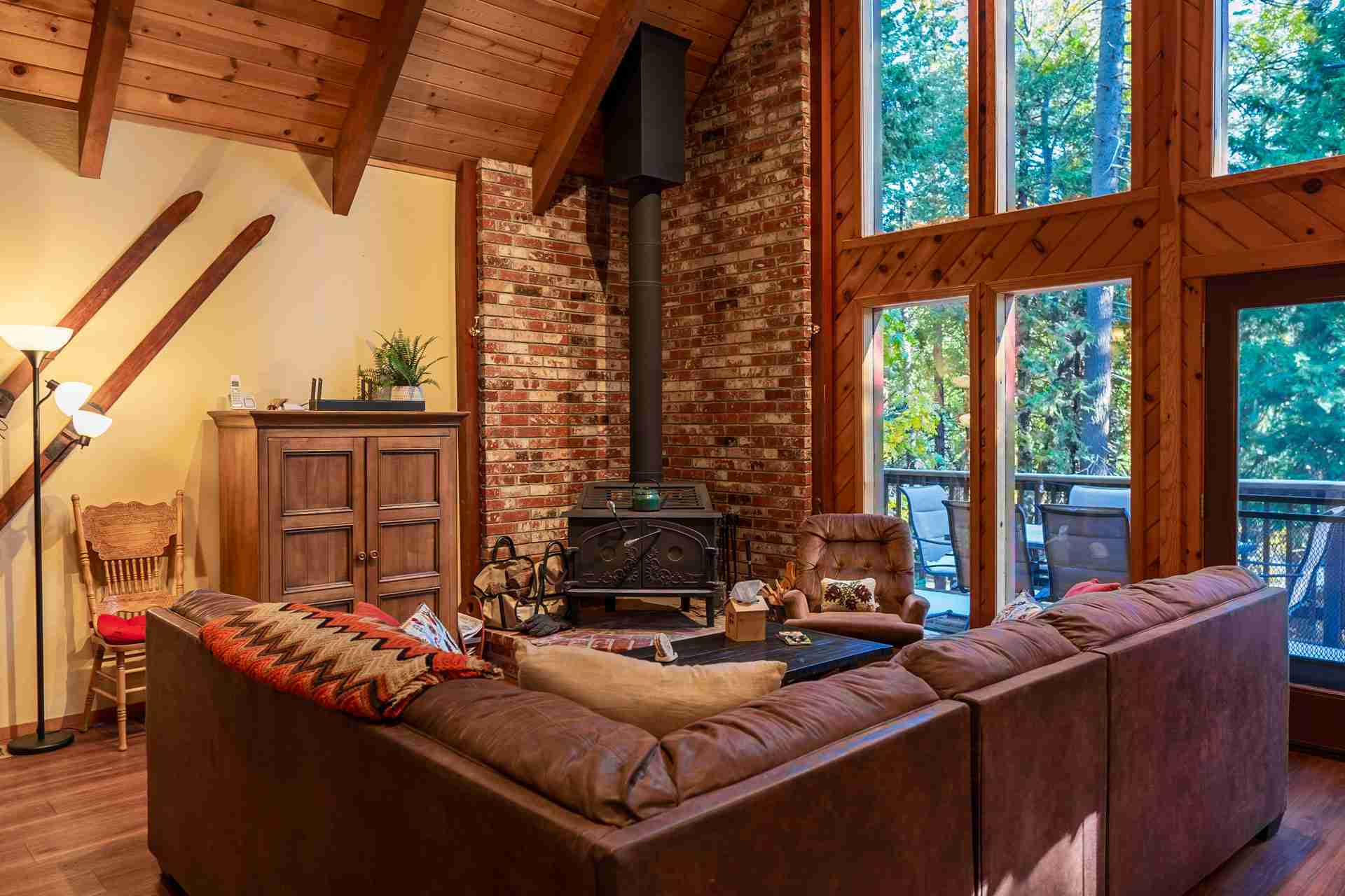Cozy living room with rustic design, brown sofa, wood stove, brick wall, and large windows.