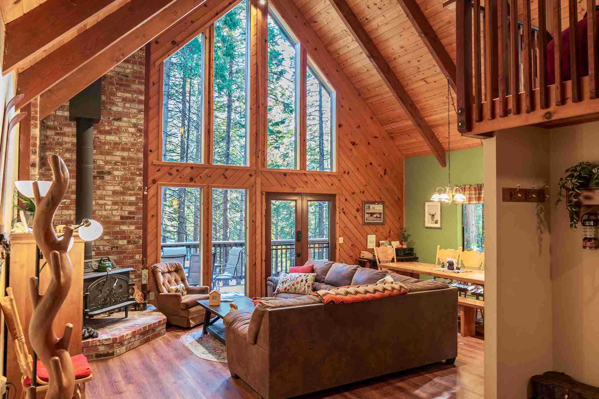 Cozy living room with high ceiling, triangular windows, fireplace, sofa, and dining area.