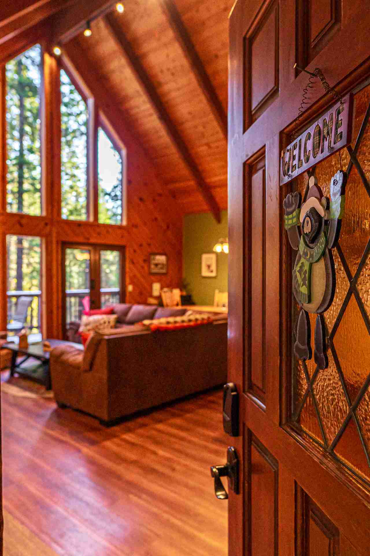Wooden cabin interior with a couch, table, and forest view through large windows.