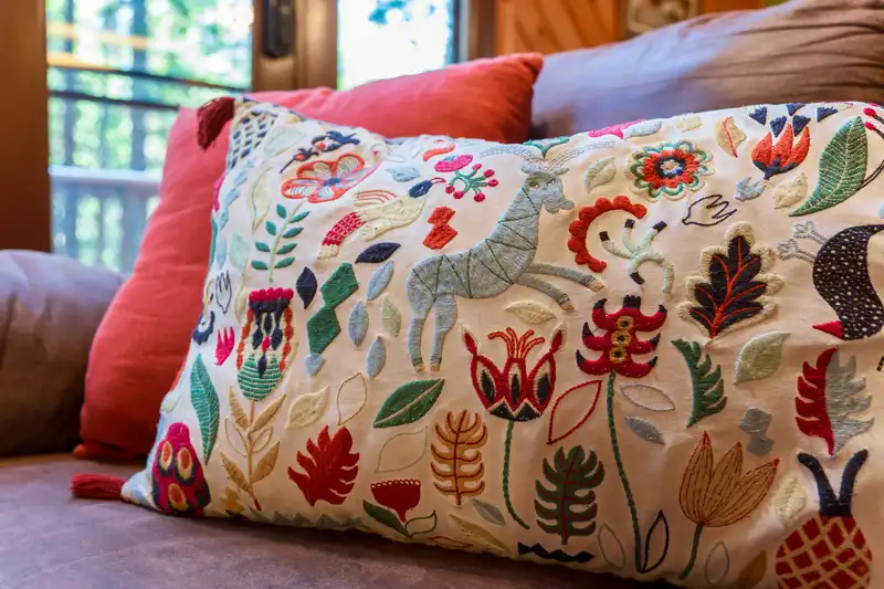 vacation rental cabin A decorative pillow with colorful, embroidered floral and animal patterns adds comfort to the space, sitting on a brown sofa with an orange cushion in the background—perfect for a cozy Chalet vibe. near Arnold California